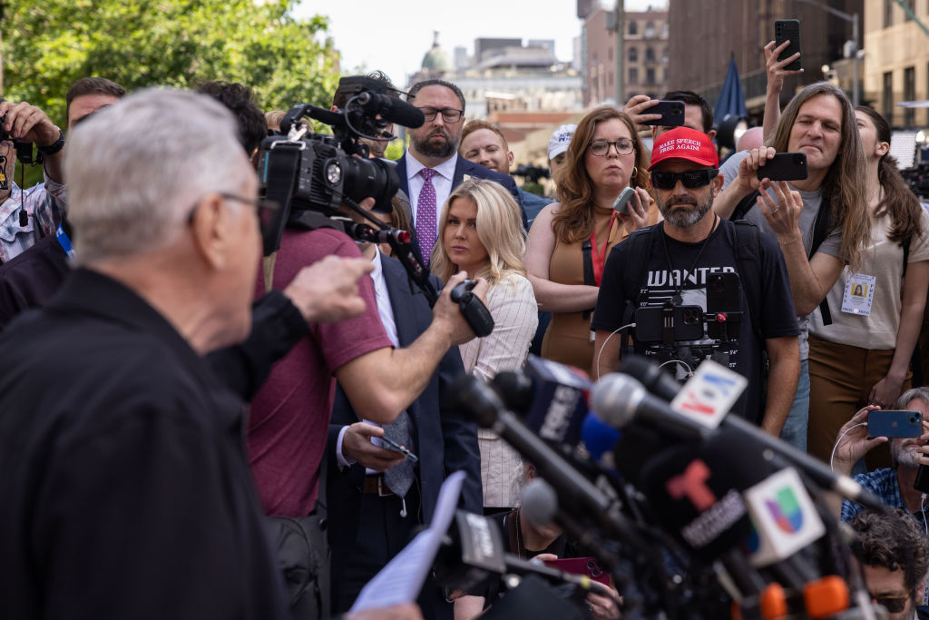 Actor Robert De Niro, standing at a podium, points to supporters of former President Donald Trump during a news conference outside Manhattan criminal court in New York,