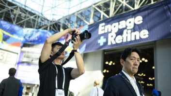 A visitor takes a photo in the lobby of the Javits Center in New York under a sign that says Engage and Refine.