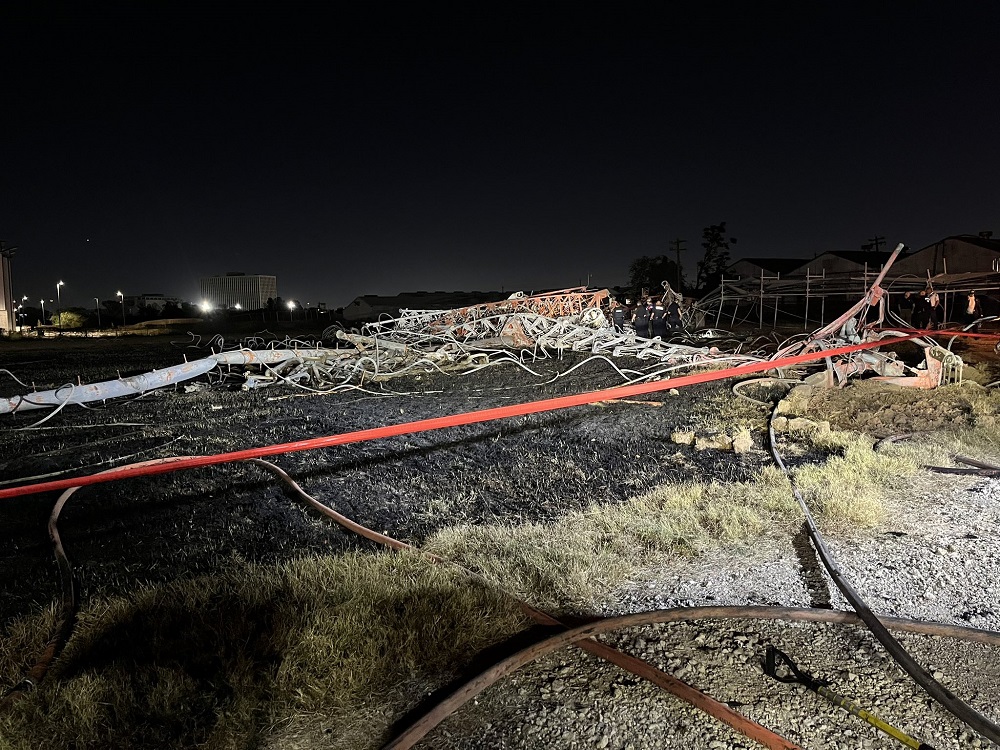 A communications tower lies crumpled on the ground in a nighttime photo.