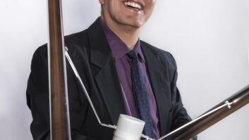 A man smiles while holding an FM antenna element. He is wearing a suit and tie.