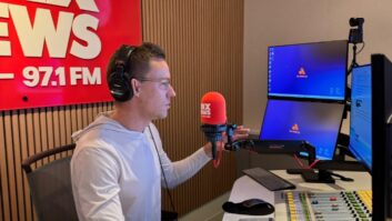 A man sits at a microphone in a radio studio, with a sign behind him that says "KNX News 97.1 FM"