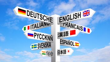 Multilingual languages and flags sign post against blue sky.