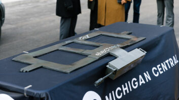 A flat metal device sits on a display table at a press conference.